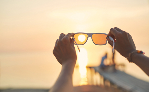 Hands holding up sunglasses against the sun, illustrating the importance of UV protection for long-term eye health