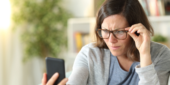 Woman squints at a smartphone held up in front of her, holding her glasses and frowing to illustrate presbyopia.