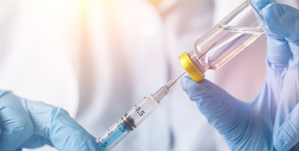 Close up of gloved hands extract a syringe of medication from a vial.
