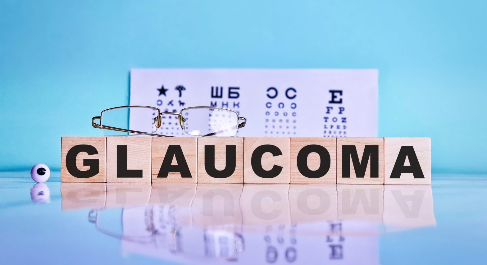 Blue background with an eye test paper resting against it. In the foreground, wooden blocks spell out the word GLAUCOMA.