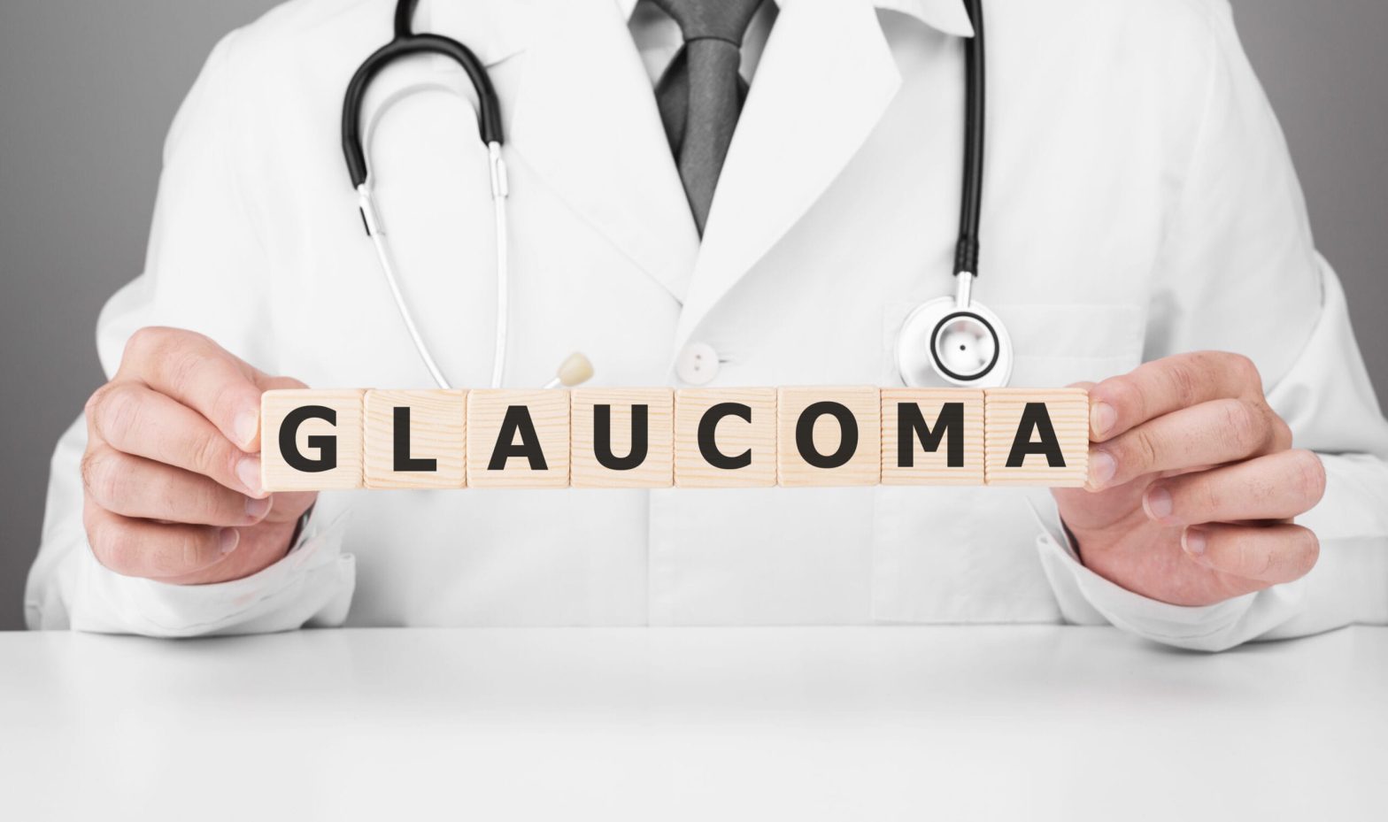 Man wearing white lab coat with a stethoscope around his neck holding up wooden blocks spelling GLAUCOMA